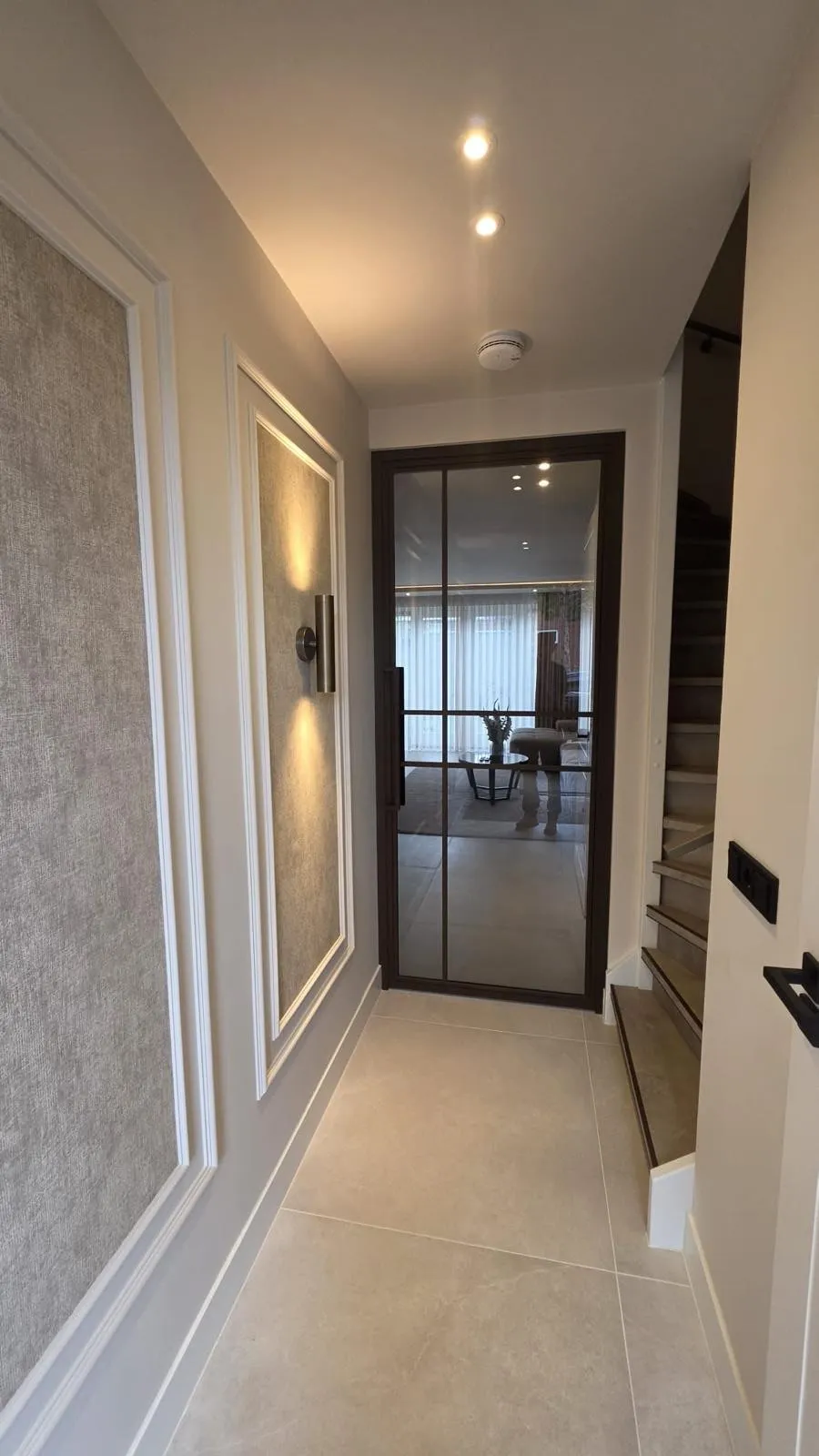 Hal met sierlijsten op de wanden, een stalen deur met glas naar de woonkamer en een trap naar boven
