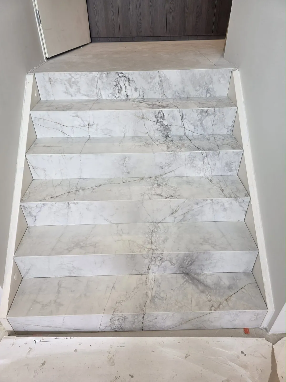 Trap bekleed met marmerlook tegels, gezien van onderaf, met een houten deur bovenaan